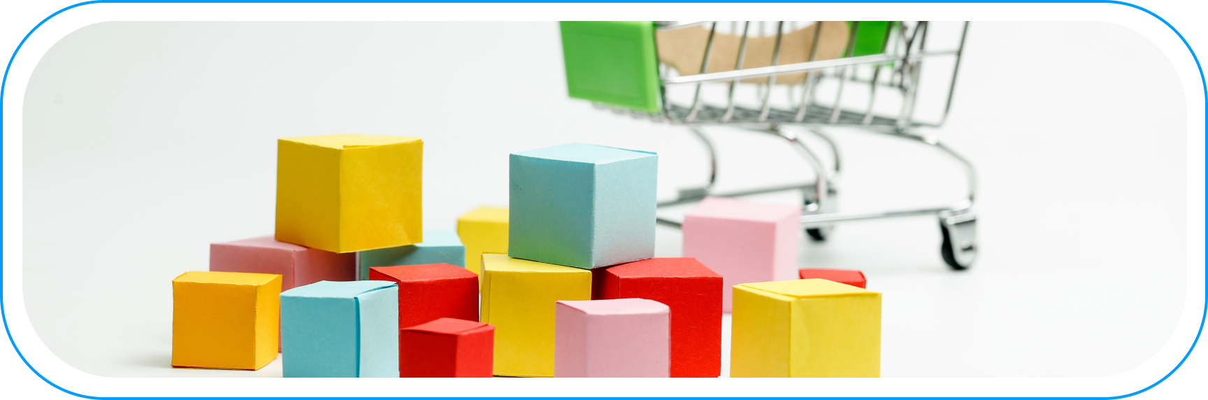 Kolorowe pudełka symbolizujące zapasy w e-commerce na tle miniaturowego wózka zakupowego — wizualizacja zarządzania zapasami.